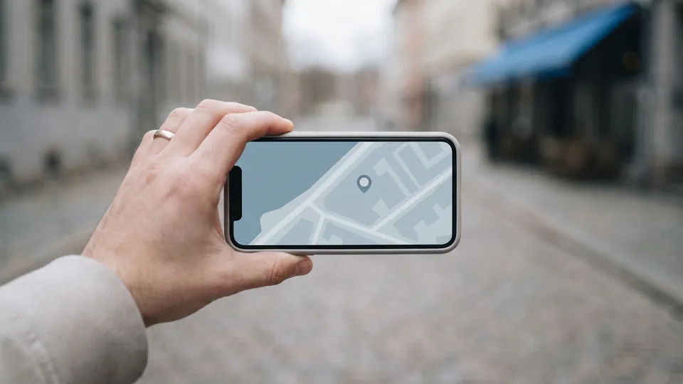 Mão segurando um celular que mostra um mapa com um marcador de local, numa rua de paralelepípedo desfocada